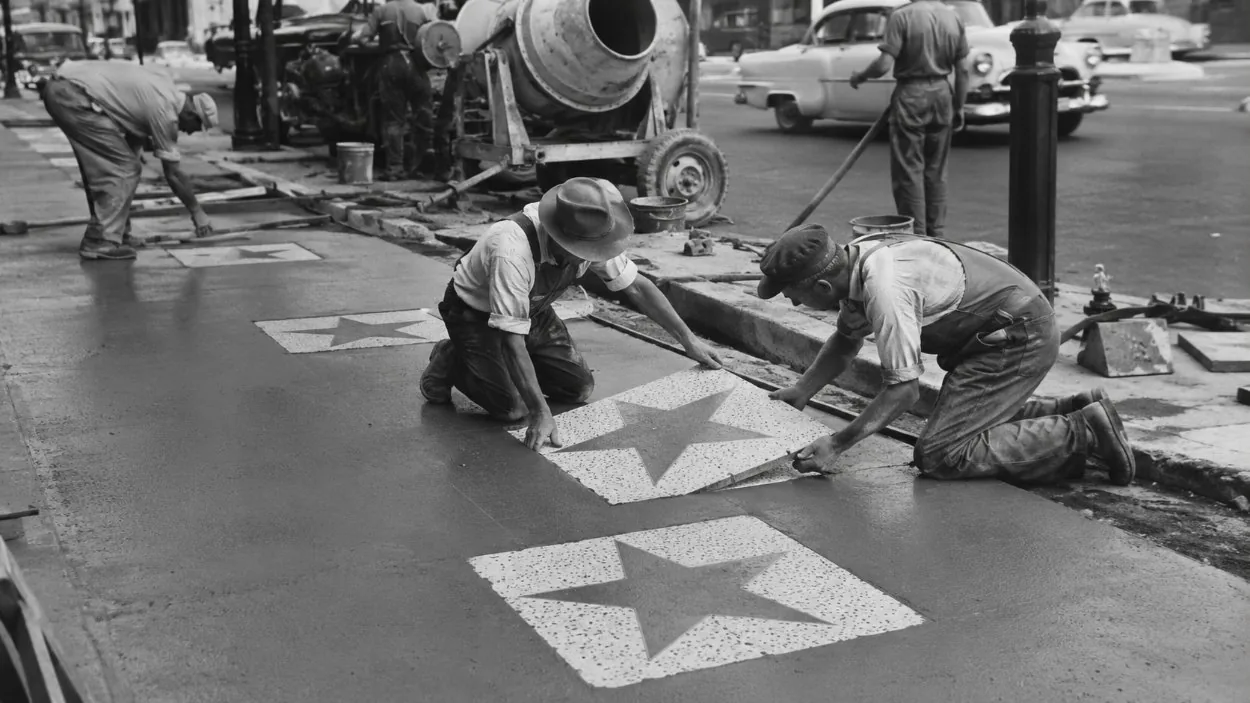 Una scena in bianco e nero d’epoca con operai che posizionano le stelle in un nuovo marciapiede